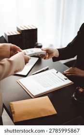 Hands exchanging a stack of us hundred-dollar bills over a contract and legal books, depicting bribery, clandestine payment and white-collar corruption in a law or office setting