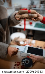 Hands exchanging wrapped gifts and processing a contactless payment for holiday shopping using a credit card terminal