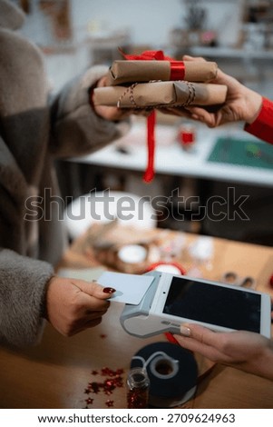 Hands exchanging wrapped gifts and processing a contactless payment for holiday shopping using a credit card terminal