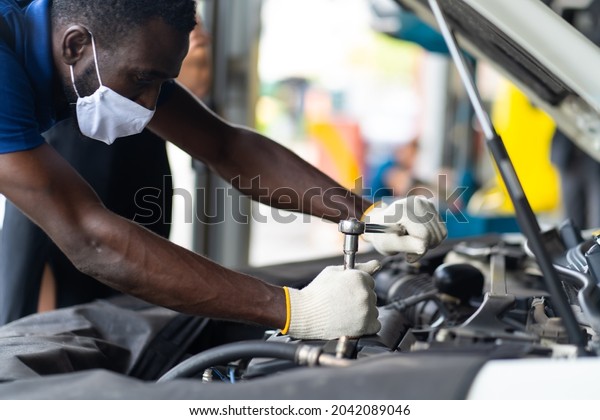 Hands Expertise car mechanic in auto\
repair service. Car maintenance and auto service garage concept.\
Black man wearing medical face mask protec virus\
corona