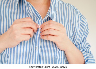 hands fasten the wrong button of blue and white striped shirt , represent the concept of getting the first button right and all the others will be in line, selective focus on the tip of the finger