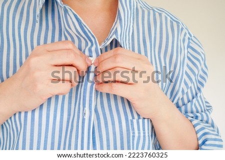 hands fasten the wrong button of blue and white striped shirt , represent the concept of getting the first button right and all the others will be in line, selective focus on the tip of the finger