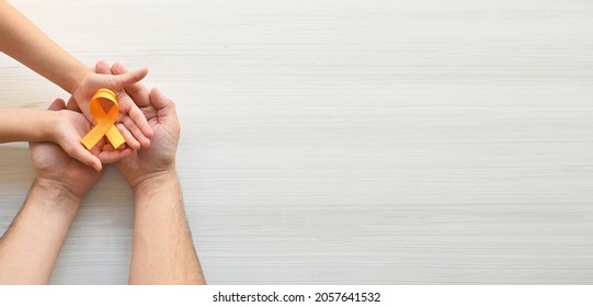 Hands Of Father And Child Hold Orange Ribbon On White Background.Concept. World Multiple Sclerosis Day. Leukemia Cancer Awareness. COPD And ADHD. Layout. Copy Space. Banner