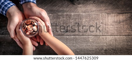 Hands Of Father Giving Jar Of Coins To Child On Wooden Table Background - Inheritance / Parent Providing For Children Concept