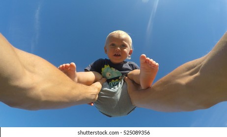 Hands of father lifts his little son on a sunny day. Dad playing with cute baby at nature. Blue sky at background. Family spends time together outdoor. POV - point of view. Close up