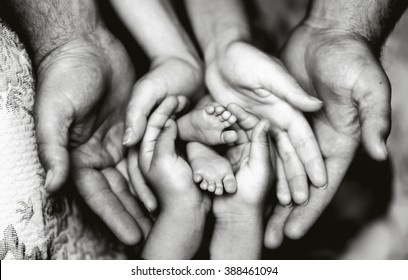 Hands of father, mother, daughter keep little feet baby. Friendly happy family, hands families together (black and white photo)