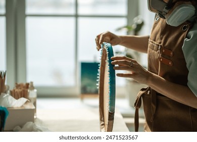 Hands of female artist work with epoxy resin painting, holds round board on side. Woman going to remove hardened dried drops on back of canvas, polish artwork, bringing picture painting to perfection. - Powered by Shutterstock