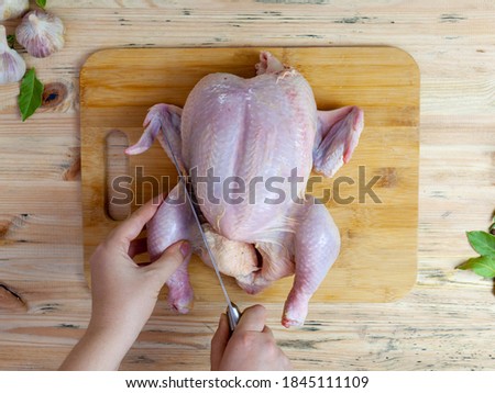 The hands of a female chef carves a whole chicken carcass on a wooden Board, the view from above. Top view