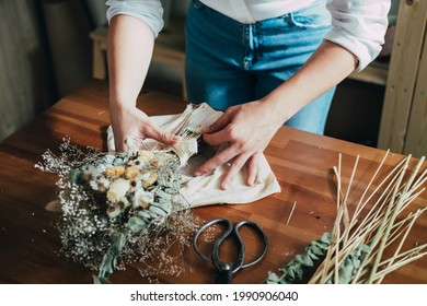 Hands of Female Florist Wrapping Everlasting Bouquet of Dried Flowers at Wooden Table at her Flower Shop.
High angle view of unrecognizable woman entrepreneur arranging bouquet of a dry flowers. - Powered by Shutterstock