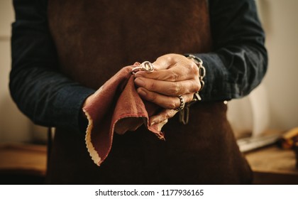 Hands of female jeweler polishing silver old-fashioned jewelry with a cloth. Jewelry maker wiping a ring with cloth at her workshop.