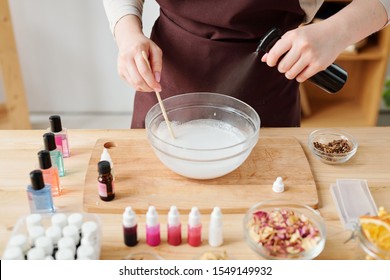 Hands Of Female Spraying Aromatic Essence Into Liquid Mass In Glassware In Process Of Making Handmade Soap