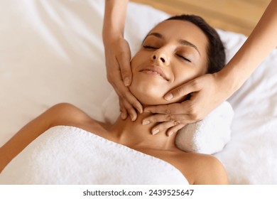 Hands of female therapist rubbing relaxed woman's chin and neck during relaxing facial massage session at spa salon indoor. High angle view of millennial lady getting healing acupuncture procedure - Powered by Shutterstock