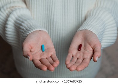 Hands of a female in a white sweater offer a choice two opposite colorful pills. Blue and red candy or meds to choose from. Concept decision making or indecisiveness. Close-up.