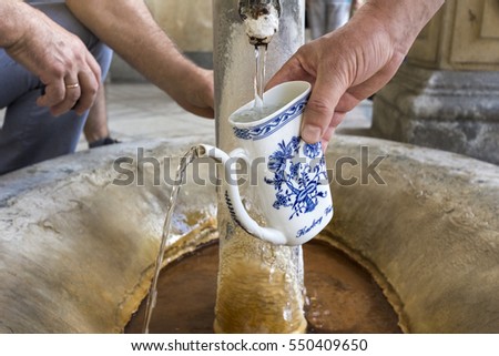 Hands fill a cup with therapeutic mineral water at a natural hot spring in Karlovy Vary, Czech Republic
