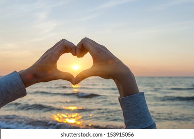 Hands And Fingers In Heart Shape Framing Setting Sun At Sunset Over Ocean