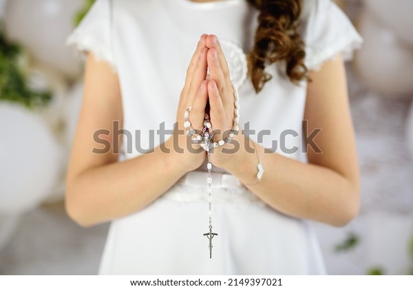 \
Hands of the First Communion girl folded in\
prayer. First Holy Communion. A girl in a white communion dress\
after receiving her First Holy Communion\
