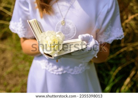 hands of a first communion girl holding a prayer book. First Holy Communion. A girl in a white communion dress. hands of a first communion girl, in white gloves, holding a Bible. outdoor prayer.