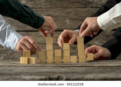 Hands of five businessman holding wooden blocks placing them into a structure. Conceptual of teamwork, strategy and business start up.