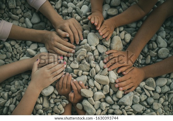 Hands of\
five children making a circle over\
pebbles.
