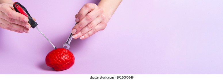 Hands fixing a model of a red brain with a screwdriver and a wrench on a pink background. Brain treatment. Fix the brain. Tools for repair