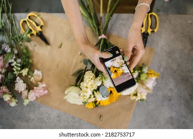 Hands Of Florist Holding Smartphone Taking Picture Of Bouquet Of Different Flowers On Counter. Flat Lay, Top View Mockup. Floristics, Business, Decoration Concept. Close Up.