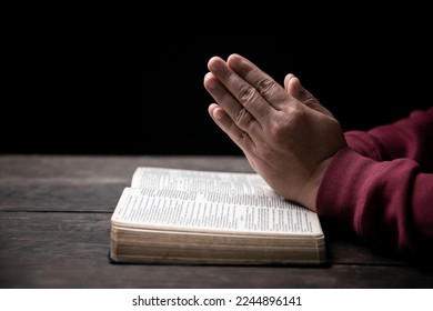 Hands folded in prayer on a Holy Bible in church concept for faith, spirituality and religion, man praying in morning. Man hand with Bible praying. Person Christian who faith in Jesus worship in dark. - Shutterstock ID 2244896141