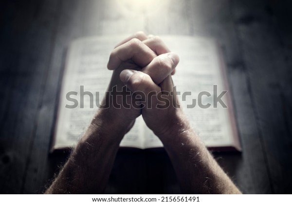 Hands folded in prayer on a Holy\
Bible in church concept for faith, spirtuality and\
religion