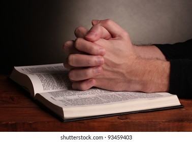 Hands folded in prayer over a Holy bible on wooden table on grey background - Shutterstock ID 93459403