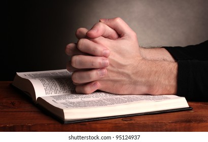 Hands folded in prayer over a Holy bible on wooden table on grey background - Shutterstock ID 95124937