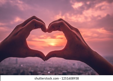 A hands in the form of heart love. Sign of valentine day at sunset with landscape view of city