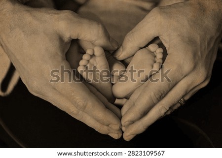 Hands forming heart around tiny baby feet in loving family moment