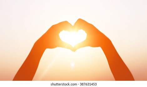 hands forming a heart shape with sunset silhouette