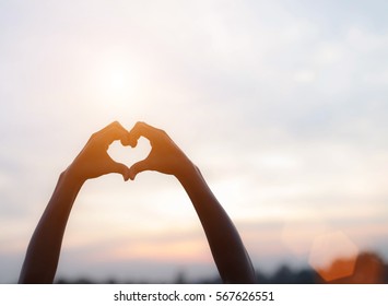 hands forming a heart shape with sunset silhouette