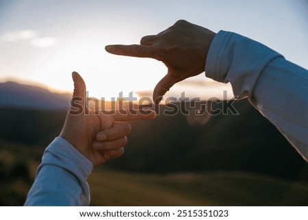 Hands in a frame shape against sunset sky