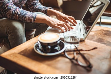 Hands Of Freelancer Woman Working Using Digital Laptop Computer And Drink Coffee Breakfast On Workplace Table At Cafe Shop In The Morning. Remote Working From Home. Freelancer Workplace In Cafe 