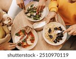 Hands of friends holding silverware while enjoying a variety of delicious dishes, including pasta, salad, and shakshuka, during a shared lunch at a restaurant