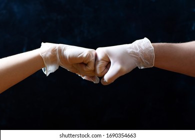 Hands of friends in medical gloves greeting each other with fist bump on black background.
