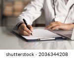 Hands of general practitioner filling paper medical records. Doctor in white coat doing paperwork at workplace with laptop, writing notes, preparing documents, reports, prescription. Close up