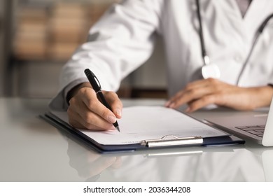 Hands of general practitioner filling paper medical records. Doctor in white coat doing paperwork at workplace with laptop, writing notes, preparing documents, reports, prescription. Close up - Shutterstock ID 2036344208