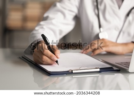 Hands of general practitioner filling paper medical records. Doctor in white coat doing paperwork at workplace with laptop, writing notes, preparing documents, reports, prescription. Close up Stock photo © 