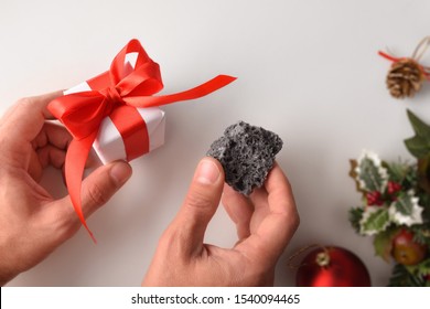 Hands With Gift And Coal On Christmas Day. Reward Concept For Good Or Bad Behavior. Horizontal Composition. Top View.