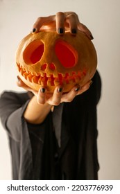 Hands Of A Girl With Black Painted Nails Holding A Halloween Pumpkin, Girl In A Black Witch Dress