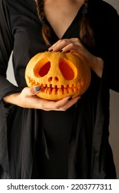 Hands Of A Girl With Black Painted Nails Holding A Halloween Pumpkin, Girl In A Black Witch Dress