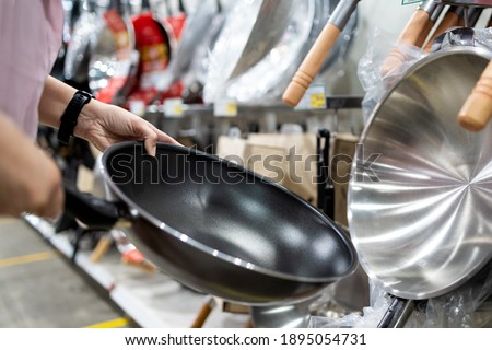 Hands of girl holding a new pan,choosing black teflon frying pan,asian  customer deciding to buy non-stick frying pan for cooking food in her kitchen,shopping cookware household goods at supermarket