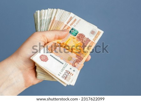 In the hands of the girl is a pack of five-thousandth and thousandth bills on a blue background close-up, selective focus. Russian, paper banknotes in their hands on a blue background. Space for text.