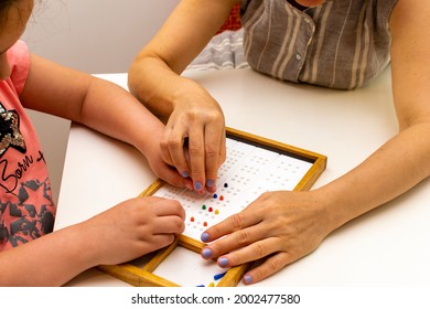 The hands of a girl and the hands of a teacher in close-up. Braille board for learning alphabet - Powered by Shutterstock