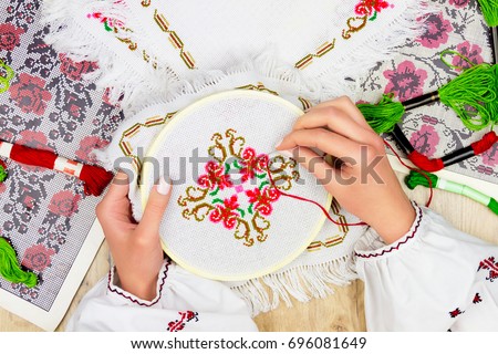 Hands of girl / woman / female in ukrainian traditional shirt sewing embroidery pattern in embroidery frame. Embroidery schemes and colorful threads on background.