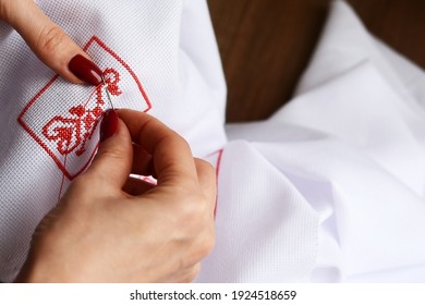 Hands Of A Girl,  Woman  Sew A Small Embroidery Pattern On A White Canvas. The Ornament Is Made With Red Floss Threads. Cross Stitch Type