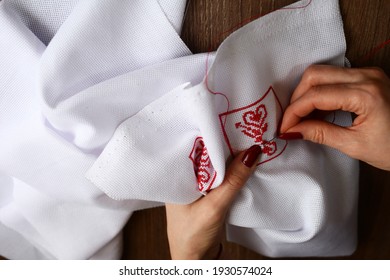 Hands Of A Girl,  Woman  Sew A Small Embroidery Pattern On A White Canvas. The Ornament Is Made With Red Floss Threads. Cross Stitch Type