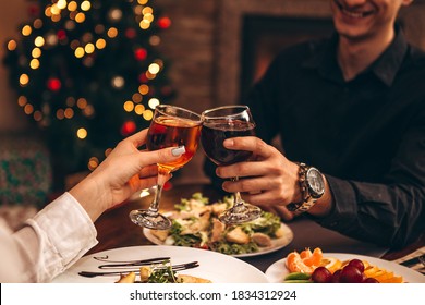 hands with glasses clinking against the background of Christmas tree lights and bonfires from a home fireplace over a table with delicious dishes
